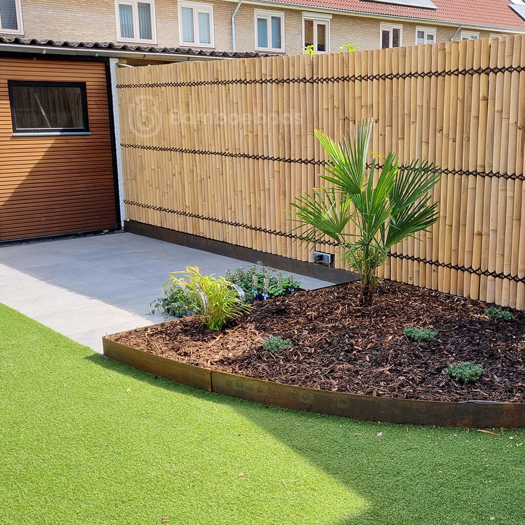 Halfronde naturel bamboe tuinschermen tegen bestaande schutting in de achtertuin